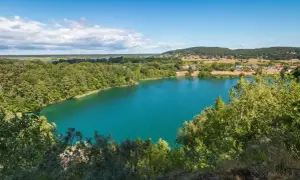 Turkusowe jezioro na Wolinie otoczone zielonymi lasami, z widocznymi domami w oddali.