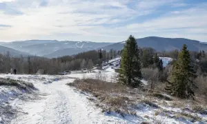 Zimowy szlak na Równicę. Śnieg pokrywa ścieżkę i zbocza, w oddali widać góry i lasy.