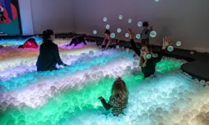 Kolorowe kulki w muzeum dla dzieci tworzą tęczową falę. Dzieci bawią się w basenie pełnym piłek, a jedna z nich rzuca je w powietrze.