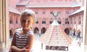 Dziewczynka w pasiastej sukience pozuje na tle zamku w Malborku, gdzie czekają atrakcje dla dzieci.
