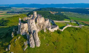 Majestatyczny zamek na skale, otoczony zielonymi wzgórzami i polami. Słoneczna Słowacja w pełnej krasie, zapraszająca do odkrywania historii.