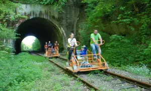 Rodzina na drezynach w Bieszczadach wjeżdża do tunelu. Wesoła wycieczka po torach wśród zieleni.