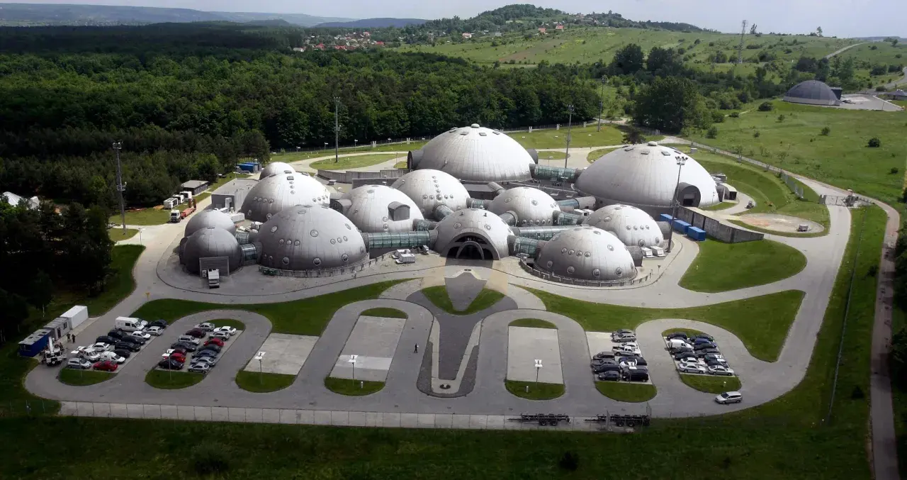 Kompleks kopuł przypominający bazę na planecie Alvernia, otoczony zielenią i lasem.