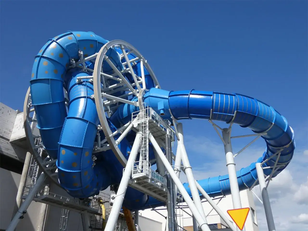 Aquapark Reda: szalona zjeżdżalnia z rekinami w kształcie pętli, niebieska, z żółtymi kropkami, na białej konstrukcji.