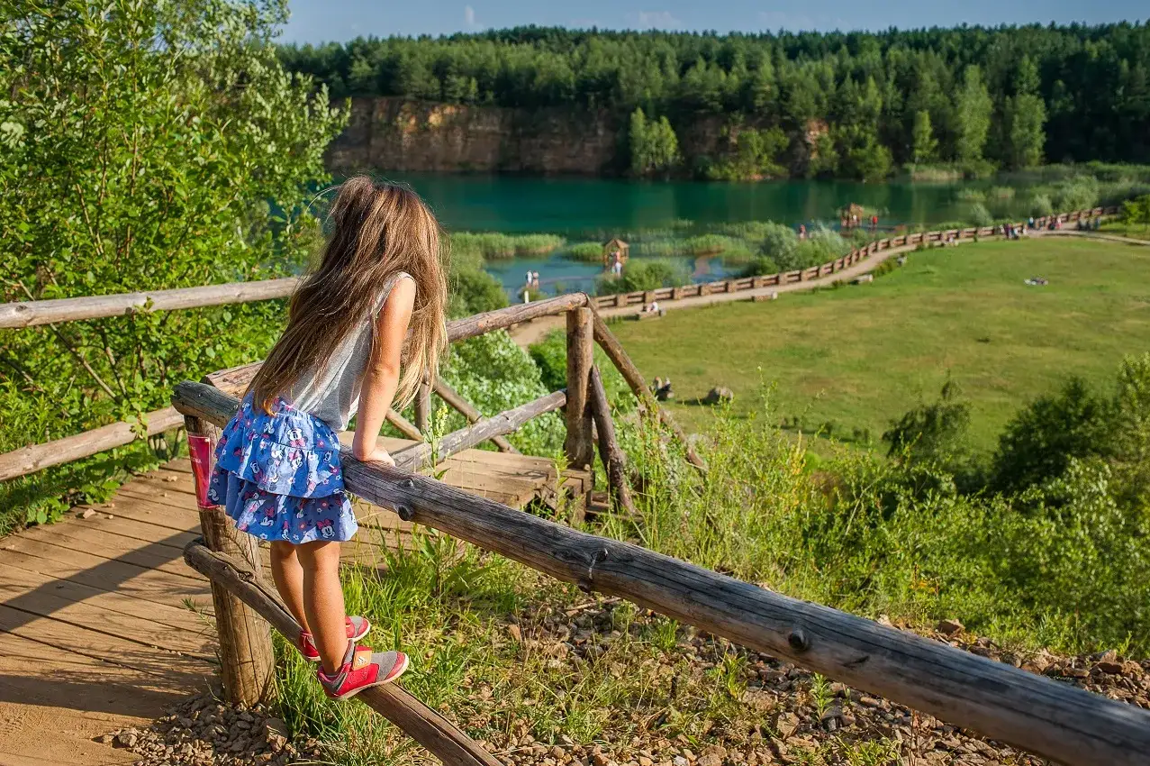 Dziewczynka z długimi włosami podziwia turkusowe jezioro i zieleń, jakby znalazła polskie Malediwy.