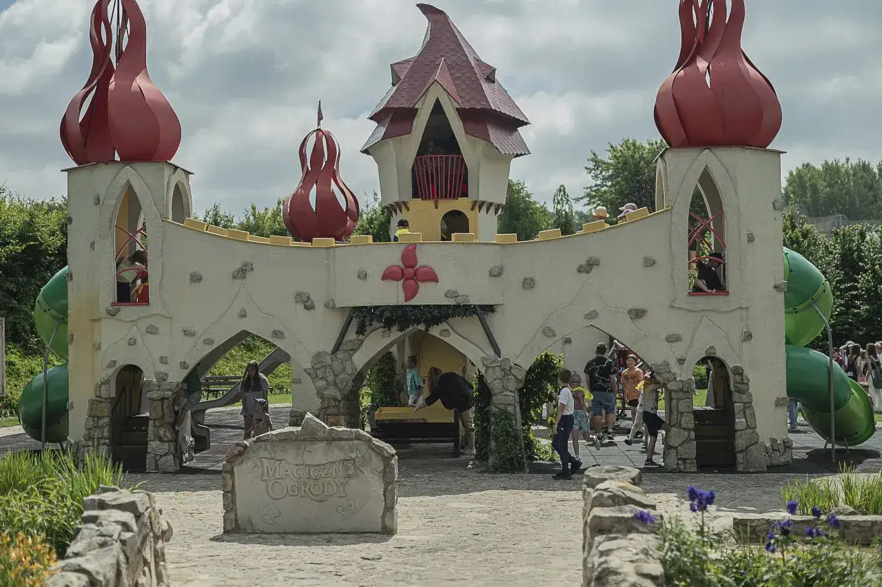 Dzieci bawią się na placu zabaw w kształcie zamku, który jest jedną z magiczne ogrody atrakcje. Zielone zjeżdżalnie i czerwone wieżyczki tworzą bajkowy klimat.