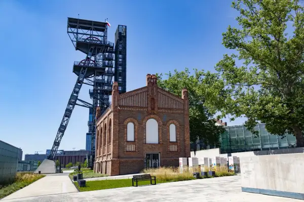Wieża szybu i ceglany budynek tworzą ciekawe katowice atrakcje dla dzieci. W tle nowoczesna architektura i zieleń.