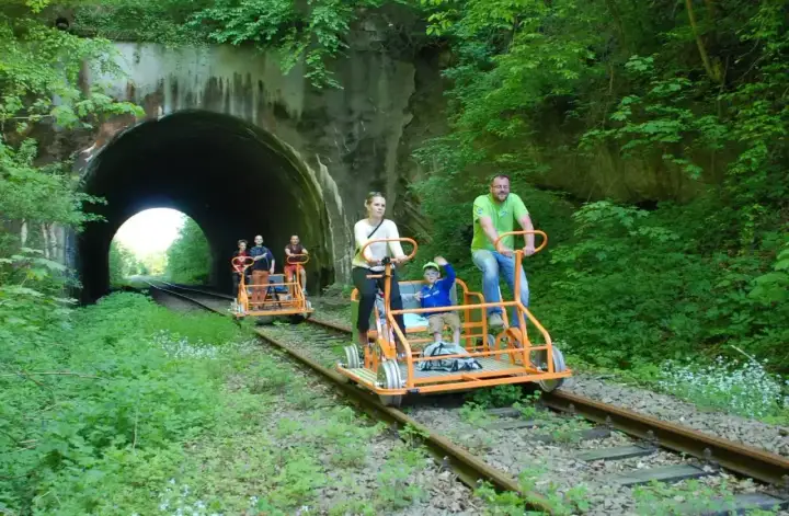 Rodzina na drezynach w Bieszczadach wjeżdża do tunelu. Wesoła wycieczka po torach wśród zieleni.
